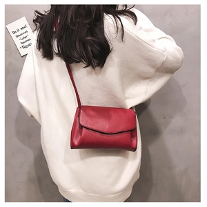 Detailed back view of a red soft leather crossbody bag on a model wearing white