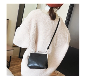 Detailed shot of vintage black kiss-lock crossbody bag worn over a soft white sweater