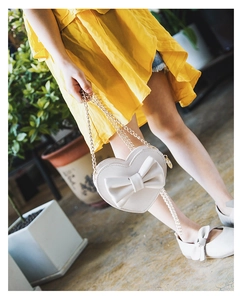 Close-up of heart-shaped cream kid handbag with large bow and gold chain strap