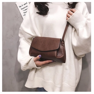Detail view of brown vintage leather crossbody bag with metal buckle on white sweater