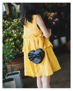 Girl in yellow dress wearing heart-shaped crossbody bag with bow and gold chain