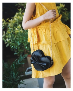 Detail of a black heart-shaped kids bag with a large bow and gold chain strap