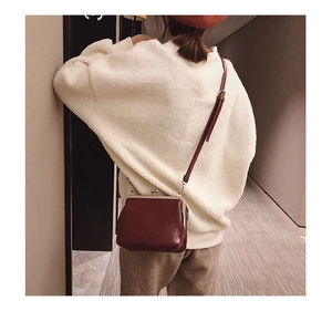 Retro burgundy leather frame bag with metal clasp worn over a white fuzzy sweater