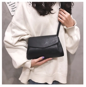 Close-up of minimalist black crossbody bag on white sweater with matte PU leather finish