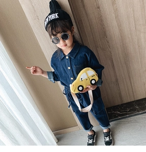 Close-up of a child wearing a yellow car-shaped canvas bag with denim jumpsuit and beanie