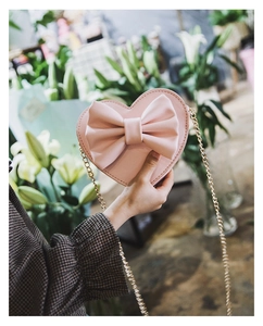 Detail of pink heart-shaped bag with large bow and gold chain strap held by hand