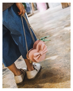 Detailed shot of a pink heart-shaped crossbody bag with a large bow and gold chain for girls