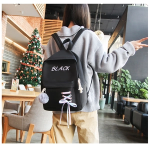 Détail d'un sac à dos scolaire noir avec lacets roses et pompon gris suspendu
