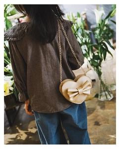 Detail of champagne gold heart-shaped crossbody bag with a large bow and gold chain