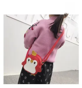 Detailed view of child wearing cartoon penguin crossbody bag in bright red leather