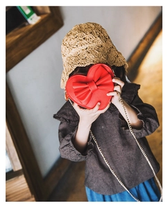 Detail of red heart-shaped kids crossbody bag with large bow and gold metal chain