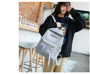 Détail de sac à dos scolaire gris avec ruban rose entrelacé et pendentif pompon doux