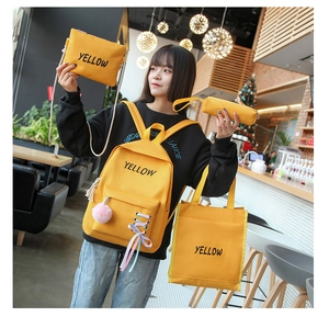 Détail d'un ensemble de 4 sacs scolaires jaunes en toile avec pompon rose et logo YELLOW
