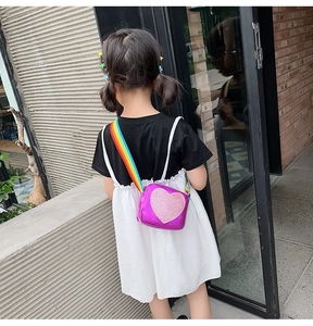 Detail of child's purple holographic heart crossbody bag with rainbow strap on a young girl