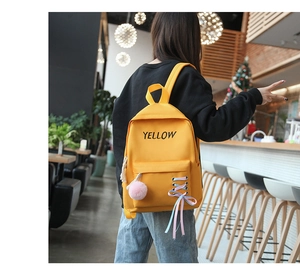 Détail du sac à dos en toile jaune avec pompon rose et ruban décoratif en nœud papillon