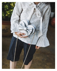 Detail of silver heart-shaped kids crossbody bag with bow and gold chain strap