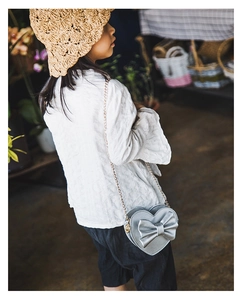 Close-up of a silver heart-shaped kids crossbody bag with a large bow and gold chain