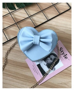 Close-up of a heart-shaped light blue bag with a large bow and gold metal chain strap