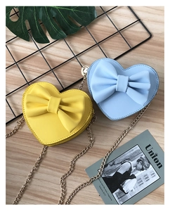Detail view of heart-shaped crossbody bags with bows and gold chains on a wooden table