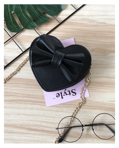 Detail of a black heart-shaped crossbody bag with a large bow and gold metal chain strap