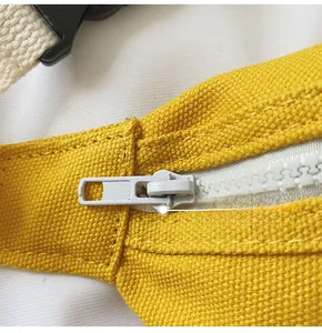 Detail of yellow canvas kids bag featuring white plastic zipper and custom metal puller