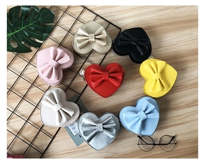 Flat lay of heart-shaped crossbody bags for kids in eight colors with bow detail