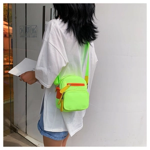 Detail of neon green nylon mini crossbody bag with orange zippers on a street model