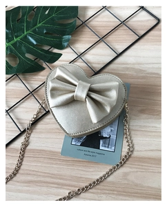 Macro detail of golden heart-shaped mini bag with large bow and fine chain strap