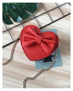 Detail of red heart-shaped children's bag with large bow and gold chain on wood surface