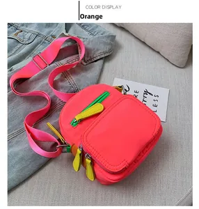 Detail view of orange nylon crossbody bag with yellow zippers on denim background