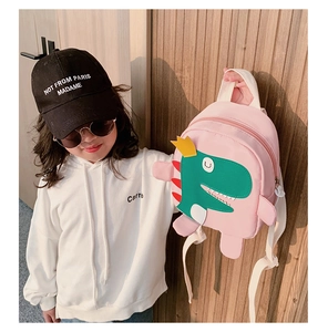 Détail d'un sac à dos rose pour enfant avec un dinosaure vert en dessin animé et couronne