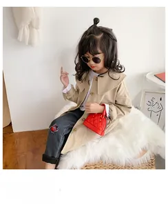 Toddler girl in khaki trench coat and grey jeans with a red quilted mini shell bag
