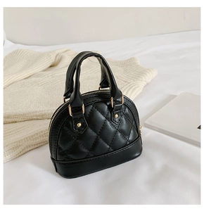 Detail view of mini black quilted shell bag with gold hardware on a cozy background