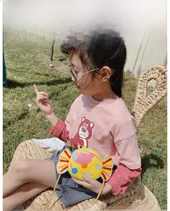 Toddler girl wearing a yellow candy-shaped crossbody bag on a bright grassy background