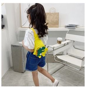 Close-up of a yellow canvas dinosaur chest bag for kids with 3D fins and a cute patch