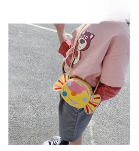 Detail of a candy-shaped yellow kids' crossbody bag with colorful dots and a gold strap