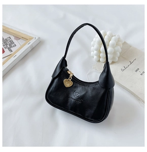 Détail d'un mini sac hobo noir en cuir avec breloque cœur doré sur un fond décoratif