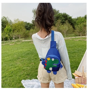 Toddler wearing royal blue dinosaur crossbody chest bag in a sunny outdoor park setting