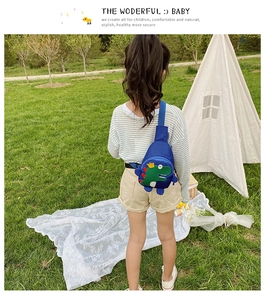 Close-up of blue kids crossbody bag with cartoon dinosaur print on a park background