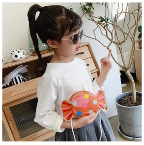 Girl wearing a bright orange candy-shaped crossbody bag with colorful polka dots