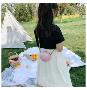 Pink basketball shaped girl's crossbody bag with gold chain strap in a park setting