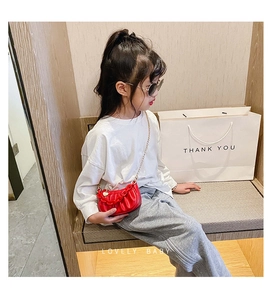 Petite fille portant un mini sac bandoulière rouge plissé avec chaîne dorée et cœur