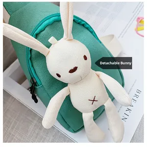 Close-up of green canvas mini chest bag featuring a detachable white plush rabbit toy