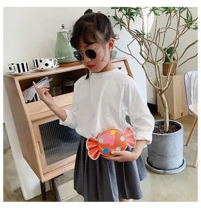 Close-up of cute orange candy-shaped crossbody bag with colorful polka dots on a child