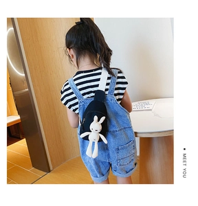 Close-up of child black canvas chest bag with cute plush rabbit pendant and white strap