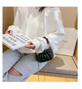 Détail d'un mini sac plissé noir avec une chaîne noire et une bandoulière dorée