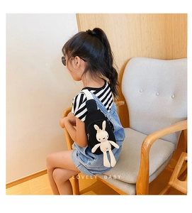 Detail view of child wearing black canvas chest bag with cute white rabbit doll