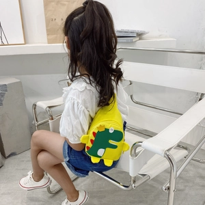 Toddler yellow canvas crossbody bag with cartoon dinosaur worn by child on white chair