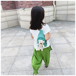 Detail view of teal canvas kids chest bag featuring a plush teddy bear charm accessory