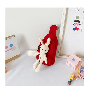 Detail showing red canvas crossbody bag with cute plush rabbit charm on a white desk